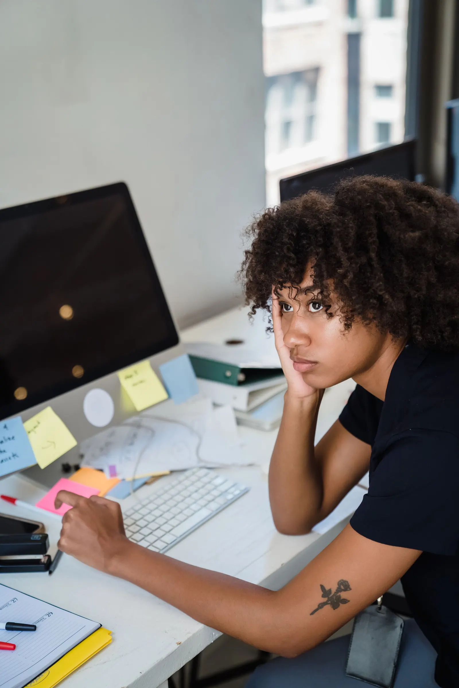 Une femme fatiguée, la tête appuyée sur la main, à son bureau