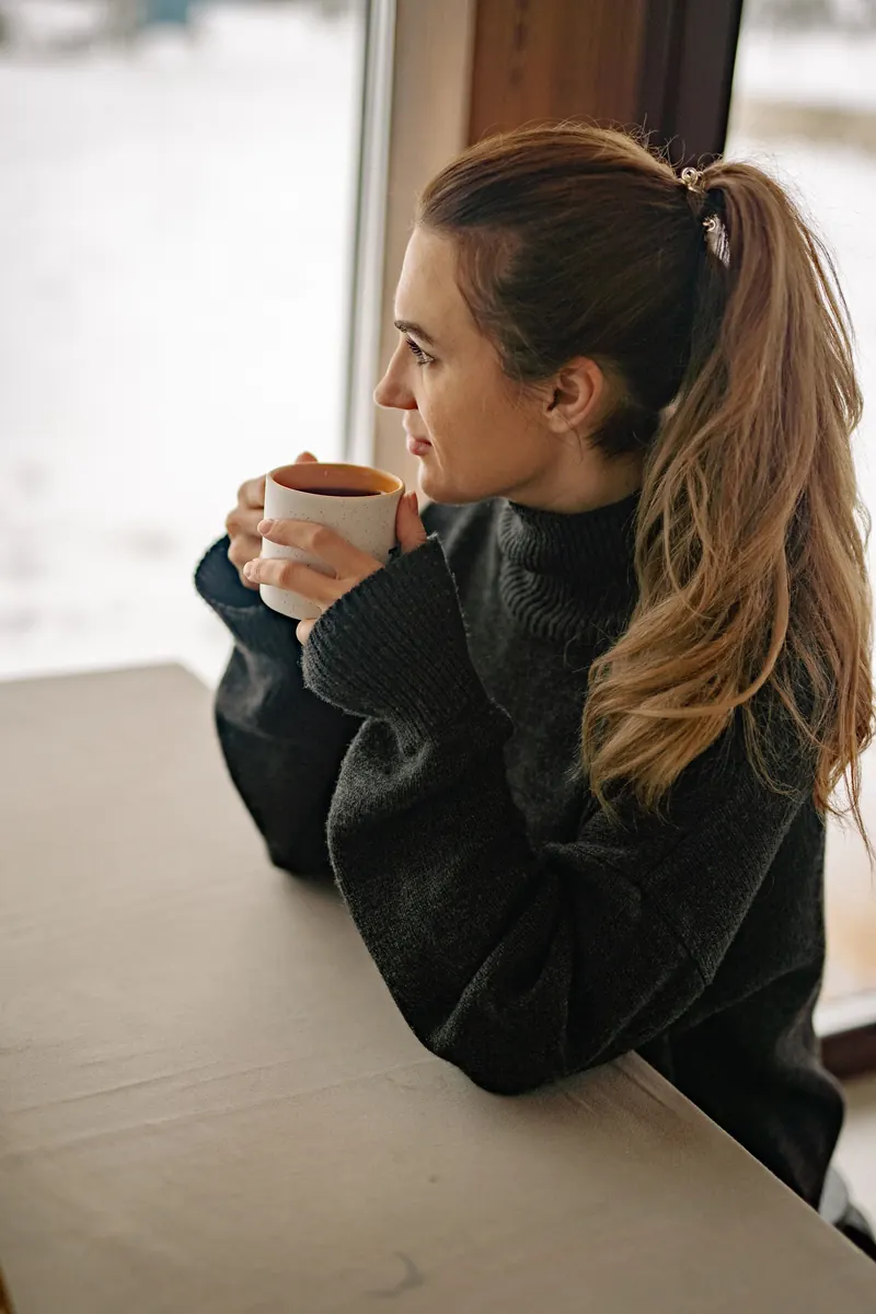 Une personne regarde par la fenêtre, une tasse à la main
